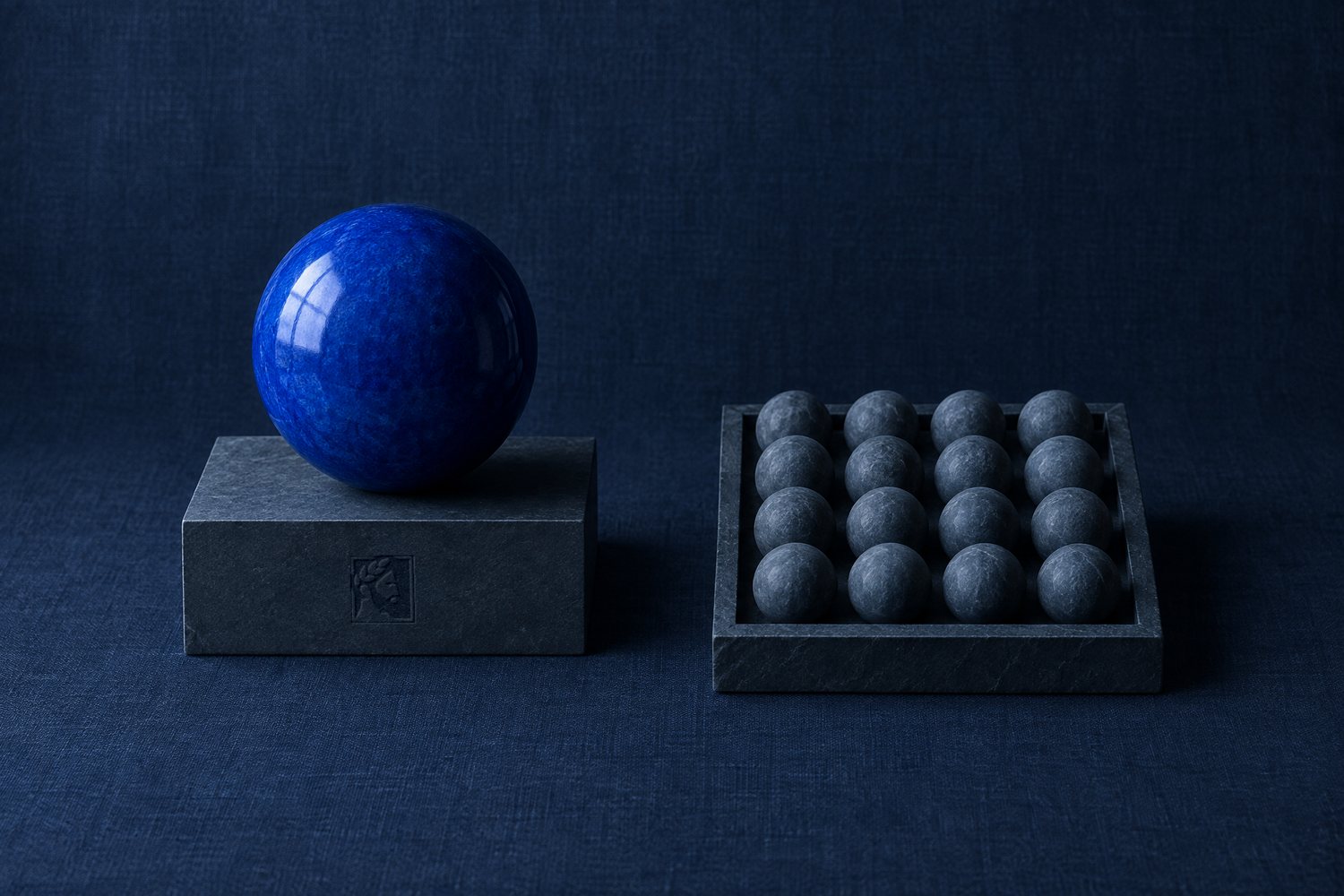 One cobalt sphere on a slate plinth pressed with the Olivent mark, beside a tray of sixteen small slate spheres