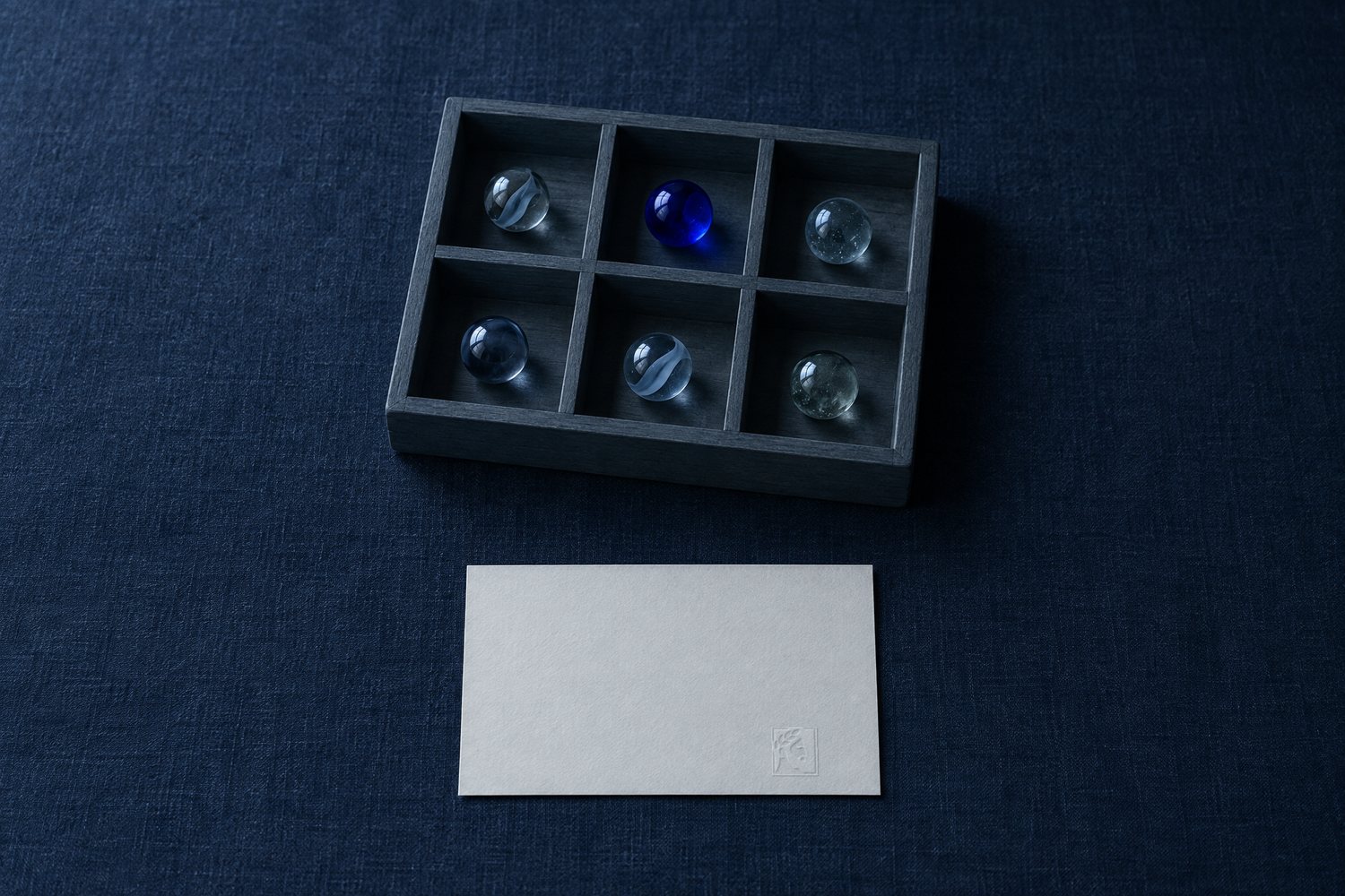 A slate tray with six walled compartments, each holding a marble, beside a white card embossed with the Olivent mark