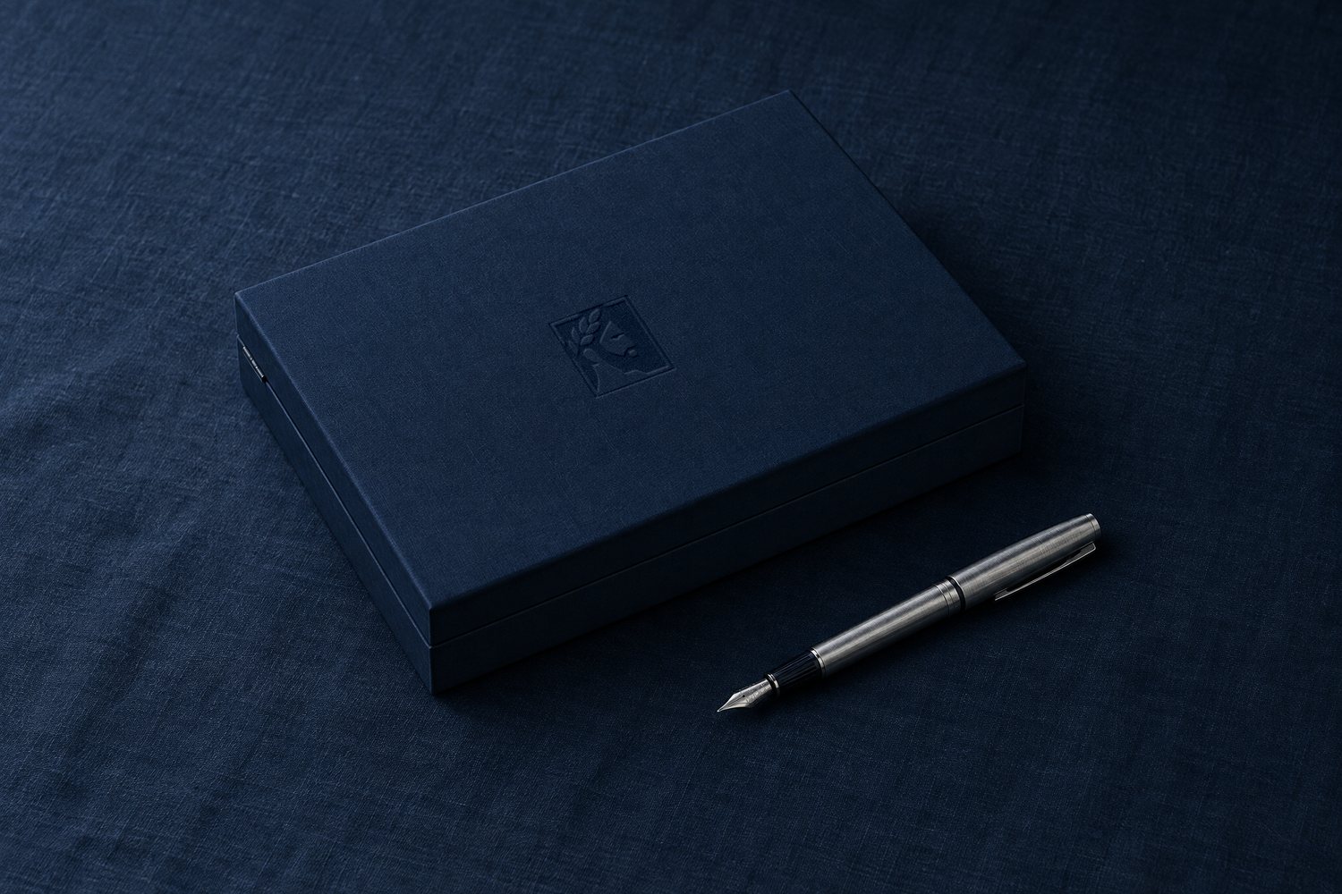 A closed navy clamshell box with the Olivent mark pressed into the lid, a steel fountain pen beside it
